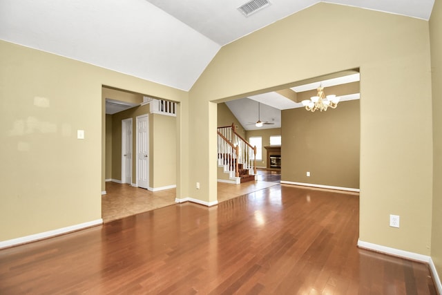 empty room featuring ceiling fan with notable chandelier, wood-type flooring, and vaulted ceiling