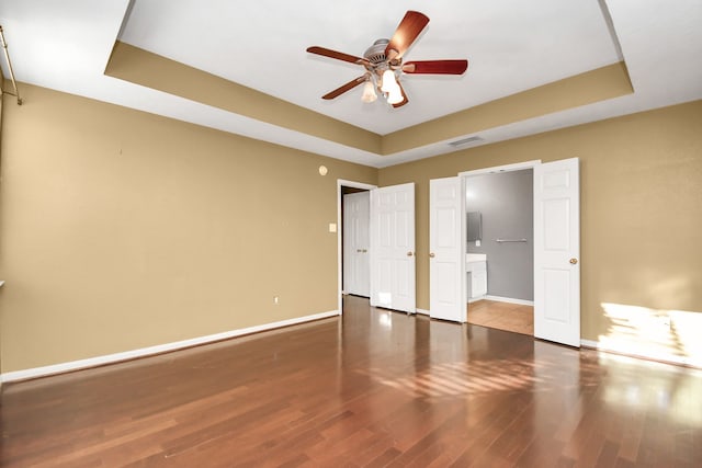 unfurnished bedroom with wood-type flooring, a tray ceiling, and ceiling fan