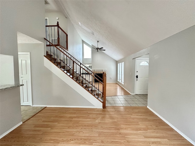 entryway with ceiling fan, light wood-type flooring, a textured ceiling, and high vaulted ceiling