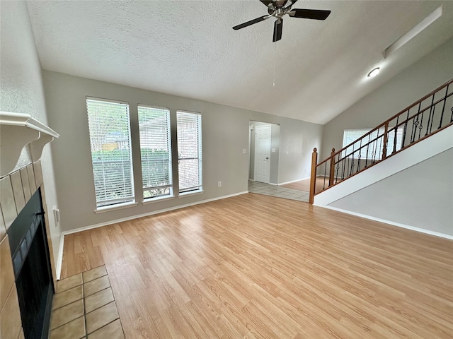 unfurnished living room with lofted ceiling, ceiling fan, a textured ceiling, light hardwood / wood-style floors, and a tiled fireplace