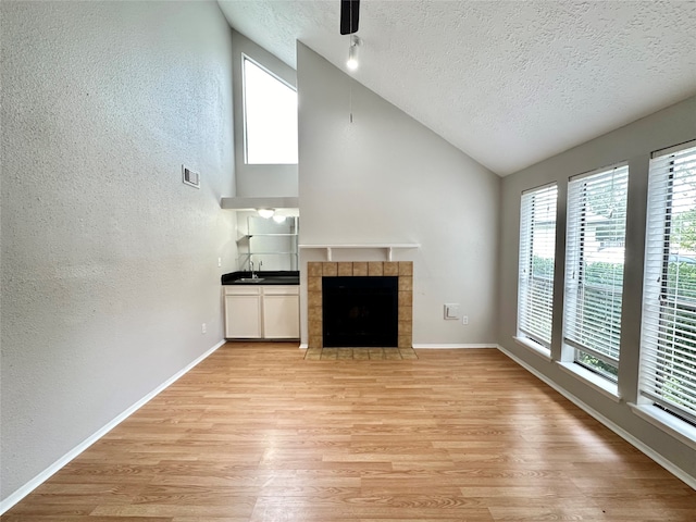 unfurnished living room with a tiled fireplace, light hardwood / wood-style flooring, high vaulted ceiling, and a textured ceiling