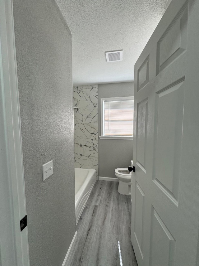 bathroom with hardwood / wood-style floors, toilet, plus walk in shower, and a textured ceiling