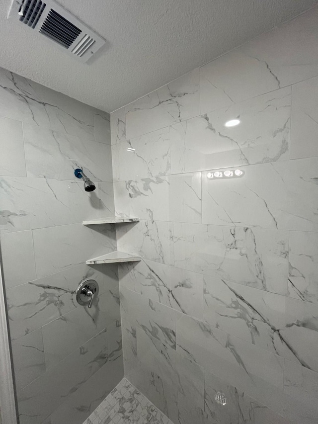 bathroom with a textured ceiling and tiled shower