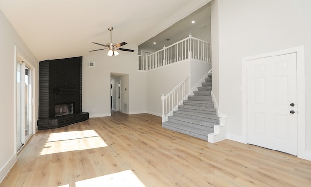 unfurnished living room featuring ceiling fan, light hardwood / wood-style floors, high vaulted ceiling, and a brick fireplace