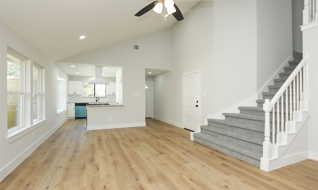 unfurnished living room with plenty of natural light, light wood-type flooring, sink, and high vaulted ceiling