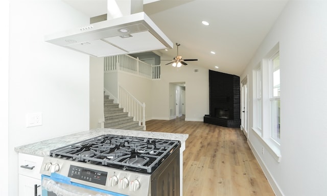 kitchen featuring light stone countertops, light wood-type flooring, ceiling fan, high vaulted ceiling, and stainless steel range with gas stovetop