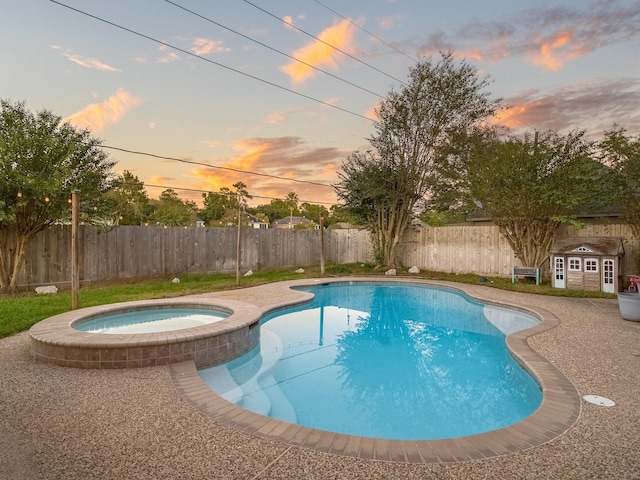 pool at dusk featuring an in ground hot tub and a storage shed