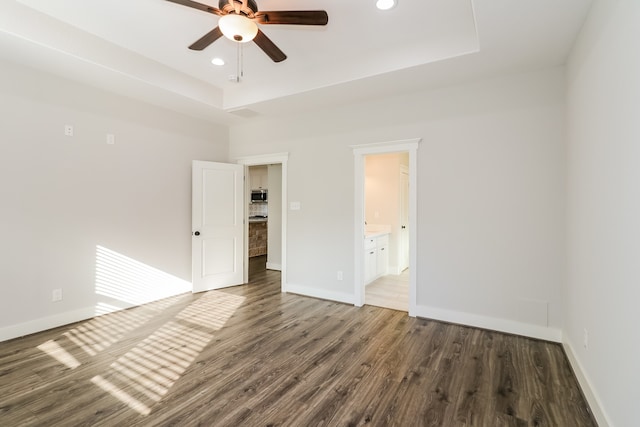 interior space with a tray ceiling, ensuite bath, ceiling fan, and dark wood-type flooring