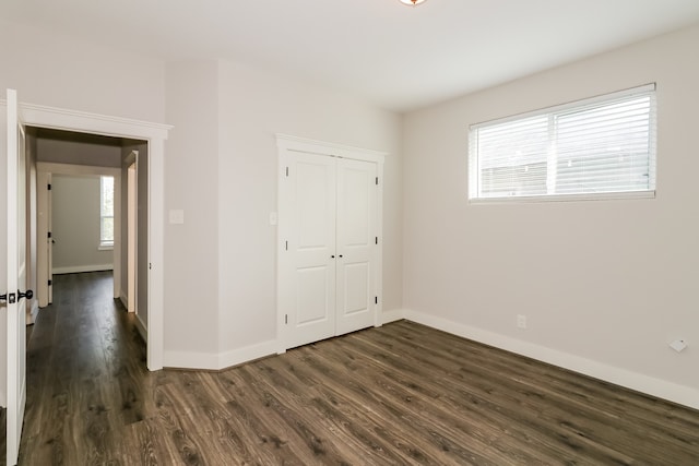 unfurnished bedroom with dark hardwood / wood-style flooring, a closet, and multiple windows