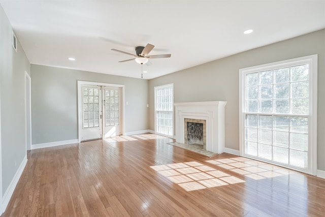 unfurnished living room with a tiled fireplace, ceiling fan, light hardwood / wood-style flooring, and a healthy amount of sunlight