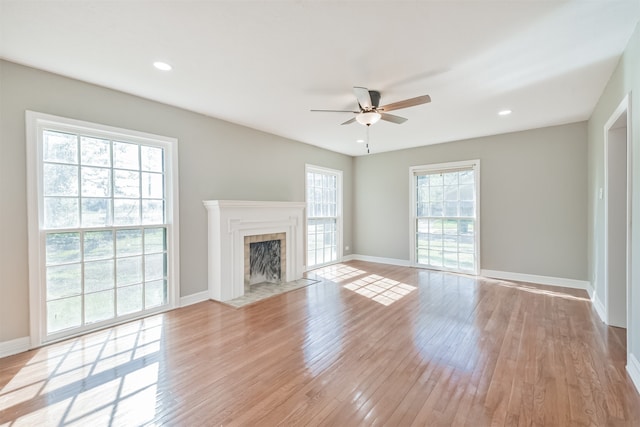 unfurnished living room featuring a tile fireplace, a wealth of natural light, ceiling fan, and light wood-type flooring