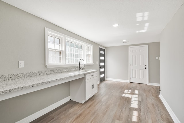 kitchen with light stone countertops, sink, built in desk, light hardwood / wood-style floors, and white cabinetry