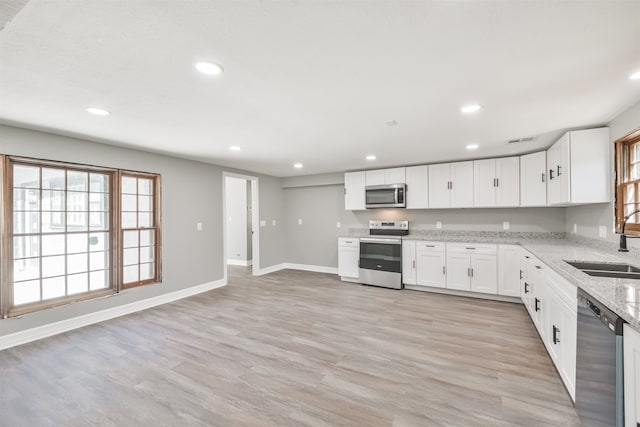 kitchen featuring white cabinets, light stone countertops, light wood-type flooring, and stainless steel appliances