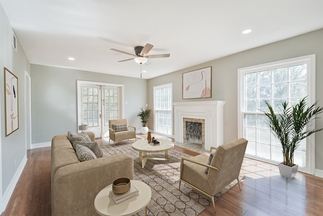 living room with ceiling fan, a tile fireplace, a wealth of natural light, and light hardwood / wood-style flooring