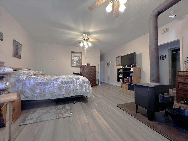 bedroom featuring a wood stove, ceiling fan, and light hardwood / wood-style flooring