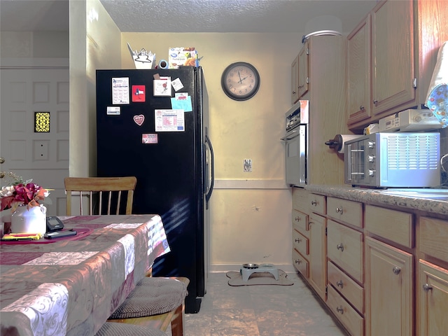 kitchen with wall oven, black fridge, light brown cabinetry, and a textured ceiling