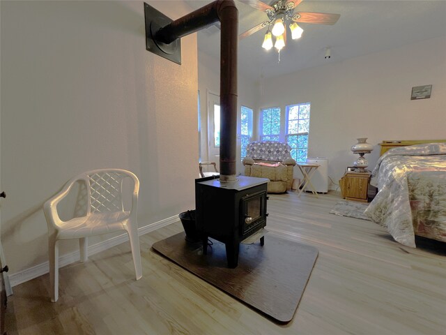 bedroom featuring a wood stove, light hardwood / wood-style flooring, and ceiling fan