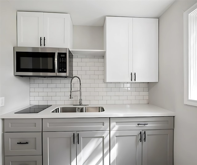 kitchen featuring black electric stovetop, backsplash, white cabinets, and sink