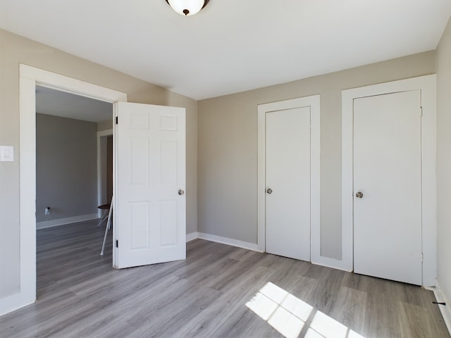 unfurnished bedroom featuring light wood-type flooring and multiple closets