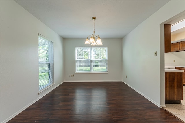 unfurnished dining area featuring a notable chandelier, plenty of natural light, and dark wood-type flooring