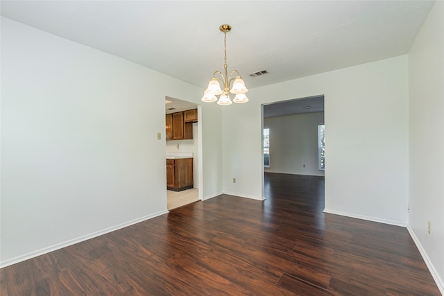 spare room with a chandelier and dark wood-type flooring