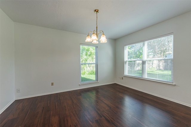 empty room with dark wood-type flooring and a notable chandelier