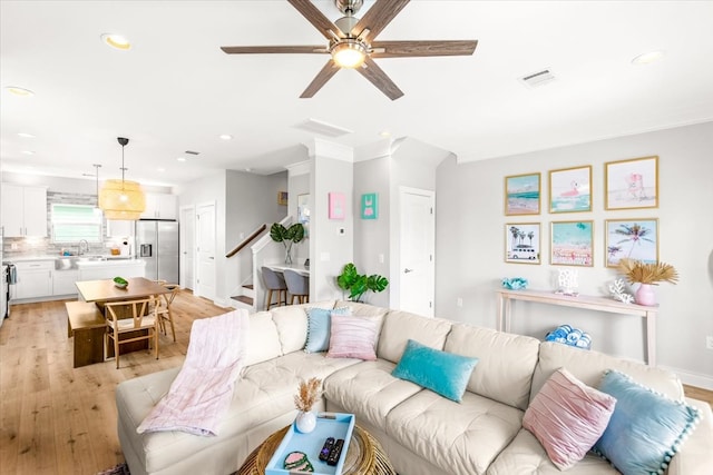 living room featuring light hardwood / wood-style floors, ceiling fan, ornamental molding, and sink