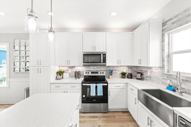 kitchen with white cabinets, sink, appliances with stainless steel finishes, decorative light fixtures, and light hardwood / wood-style floors