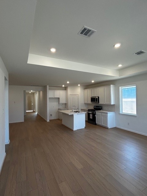 kitchen featuring black range with gas cooktop, visible vents, open floor plan, stainless steel microwave, and a raised ceiling