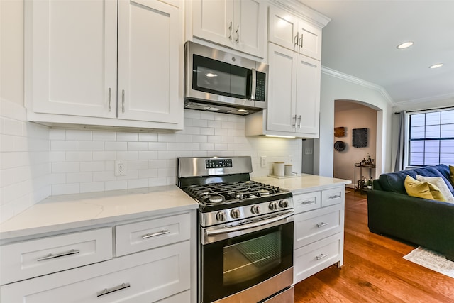 kitchen featuring crown molding, hardwood / wood-style flooring, decorative backsplash, white cabinetry, and stainless steel appliances