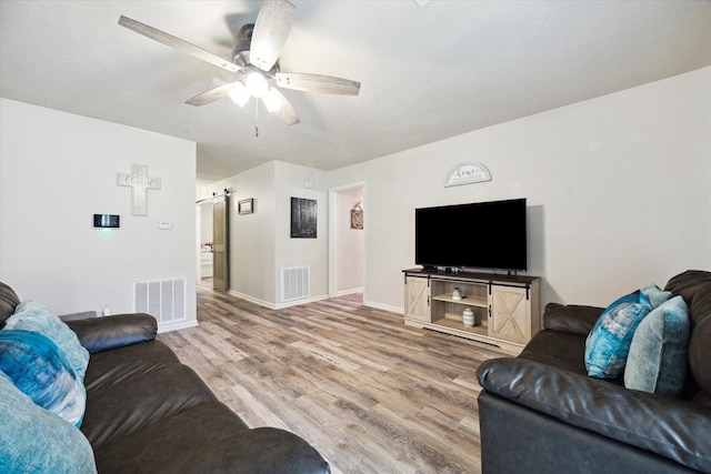 living room featuring ceiling fan, a barn door, and wood-type flooring