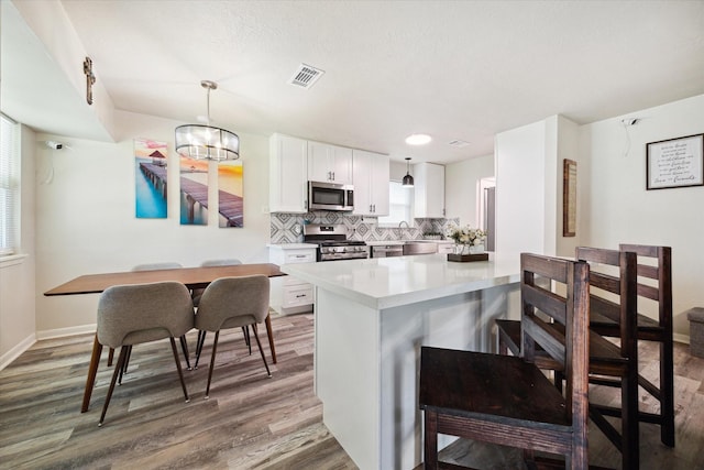 kitchen with appliances with stainless steel finishes, white cabinetry, hanging light fixtures, and plenty of natural light