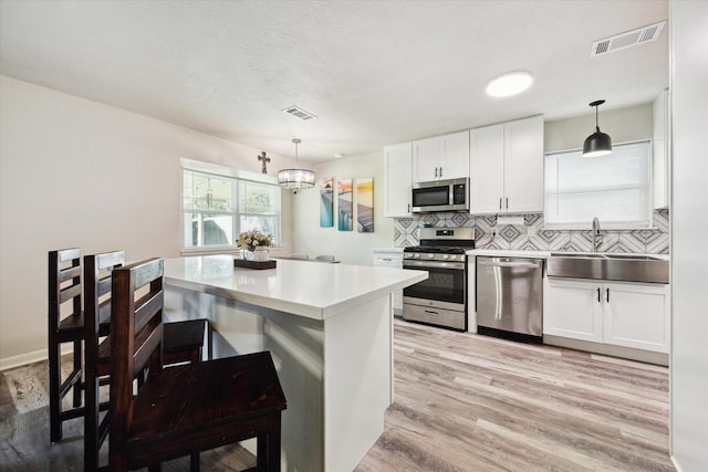 kitchen with white cabinets, sink, hanging light fixtures, light wood-type flooring, and stainless steel appliances