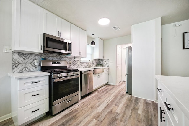 kitchen featuring white cabinets, decorative backsplash, decorative light fixtures, light hardwood / wood-style floors, and stainless steel appliances