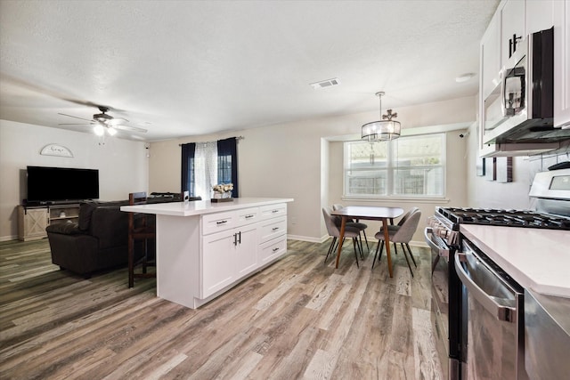 kitchen with white cabinetry, a center island, stainless steel appliances, hanging light fixtures, and light hardwood / wood-style floors