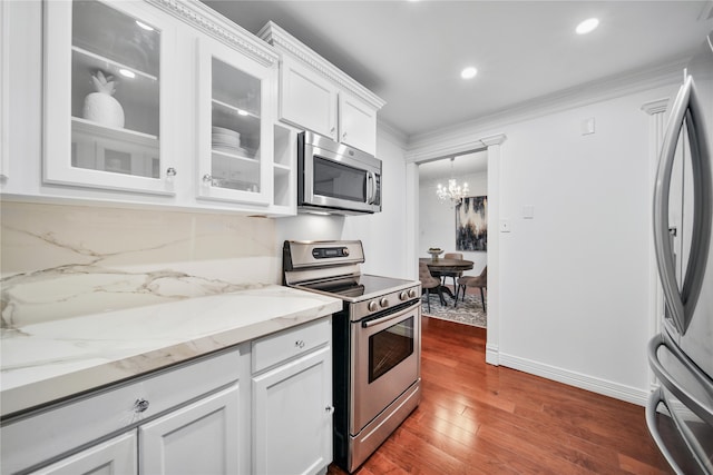 kitchen with an inviting chandelier, stainless steel appliances, white cabinetry, and dark wood-type flooring