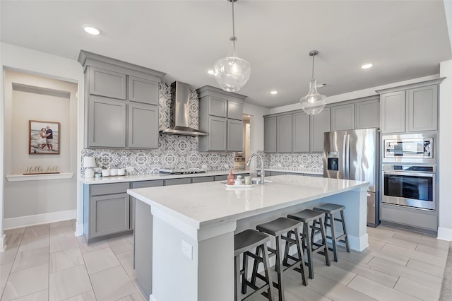 kitchen with sink, stainless steel appliances, wall chimney range hood, a kitchen breakfast bar, and pendant lighting