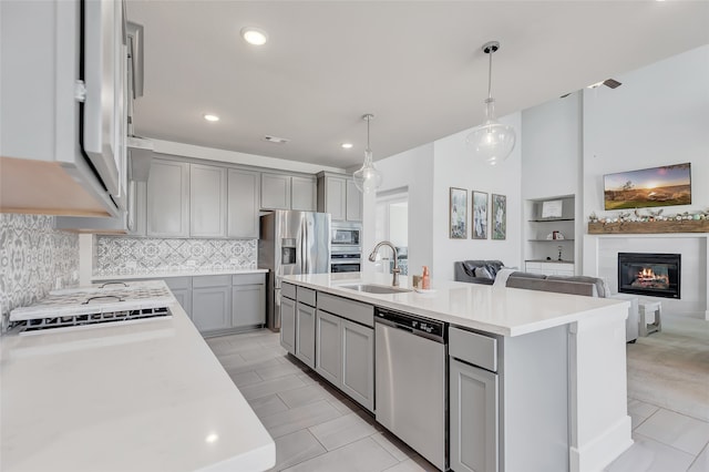 kitchen featuring appliances with stainless steel finishes, gray cabinetry, a kitchen island with sink, sink, and pendant lighting