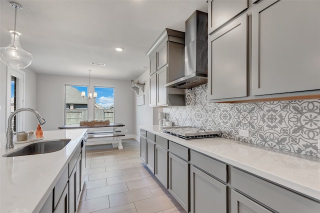 kitchen with gray cabinetry, hanging light fixtures, sink, wall chimney exhaust hood, and stainless steel gas cooktop