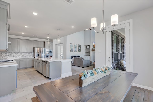 kitchen featuring decorative light fixtures, gray cabinets, a kitchen island with sink, and appliances with stainless steel finishes