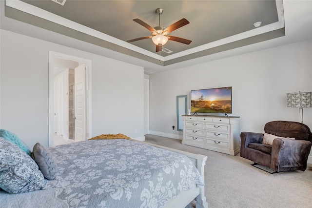 bedroom with ceiling fan, light colored carpet, a tray ceiling, and ensuite bath