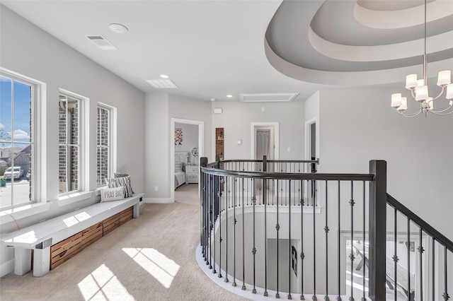 hallway with a raised ceiling, light colored carpet, and a notable chandelier