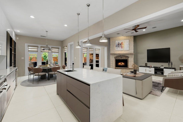 kitchen with ceiling fan, sink, a large island with sink, pendant lighting, and a fireplace