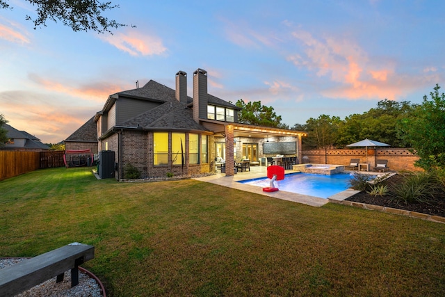 back house at dusk featuring a patio, a pool with hot tub, pool water feature, exterior kitchen, and a yard