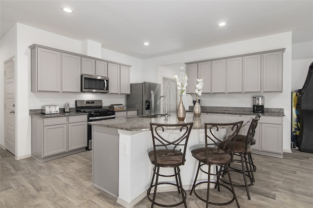 kitchen featuring gray cabinetry, a breakfast bar, stainless steel appliances, a kitchen island with sink, and light hardwood / wood-style floors