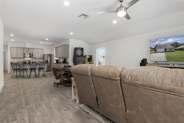 living room with ceiling fan, light hardwood / wood-style floors, and vaulted ceiling