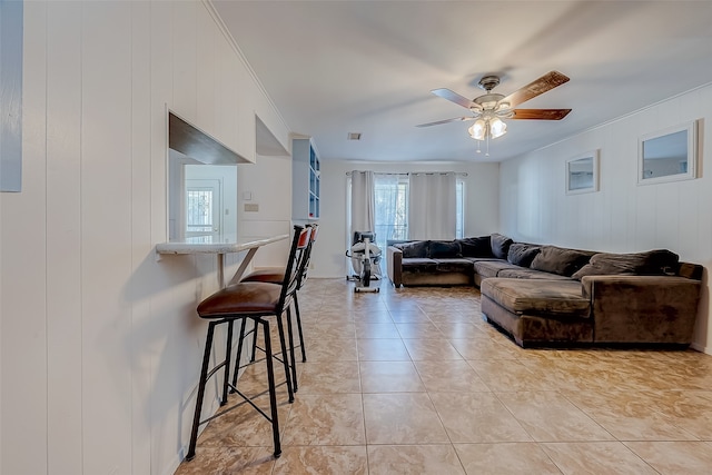 tiled living room with ceiling fan, crown molding, and wood walls