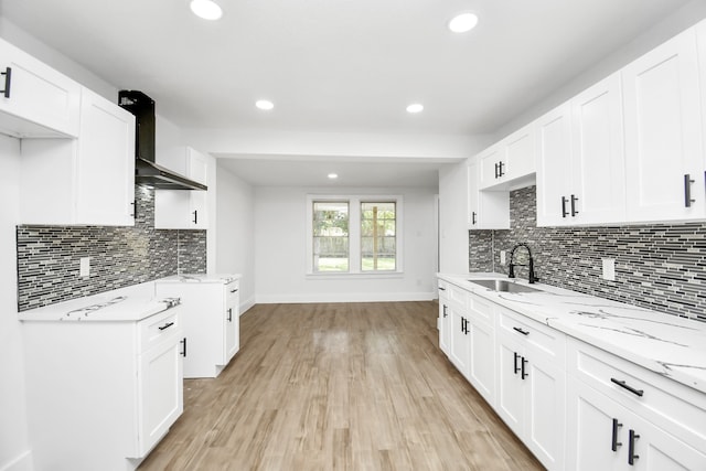 kitchen featuring light stone counters, wall chimney exhaust hood, sink, white cabinets, and light hardwood / wood-style floors