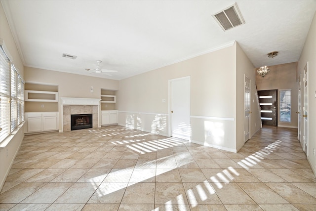 unfurnished living room featuring a tile fireplace, light tile patterned floors, ceiling fan with notable chandelier, and ornamental molding