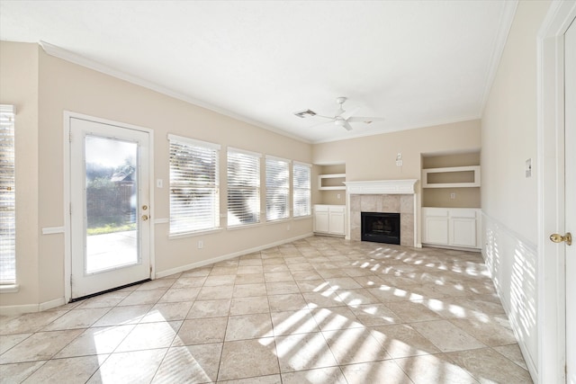 unfurnished living room featuring ceiling fan, built in features, a tiled fireplace, light tile patterned flooring, and ornamental molding